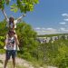A couple enjoys a playful piggyback ride on a scenic countryside hike under a sunny sky.